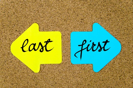 Message Last versus First on yellow and blue paper notes as opposite arrows pinned on cork board with thumbtacks. Choice conceptual imageの写真素材