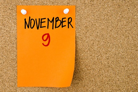 9 NOVEMBER written on orange paper note pinned on cork board with white thumbtacks, copy space availableの写真素材