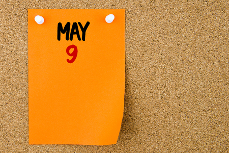 9 MAY written on orange paper note pinned on cork board with white thumbtacks, copy space availableの写真素材