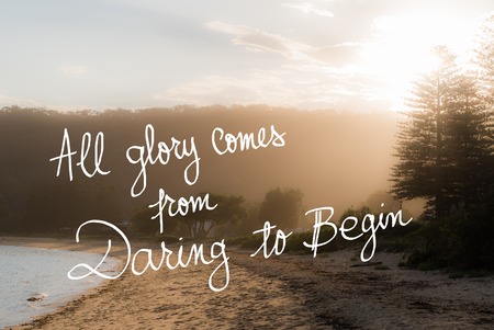 All Glory Comes From Daring To Begin message. Handwritten motivational text over sunset calm sunny beach background with vintage filter appliedの写真素材