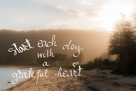 Start Each Day With A Greatful Heart message. Handwritten motivational text over sunset calm sunny beach background with vintage filter appliedの写真素材