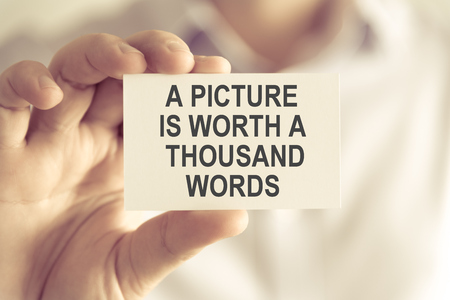 Closeup on businessman holding a card with text A PICTURE IS WORTH A THOUSAND WORDS, business concept image with soft focus background and vintage toneの写真素材