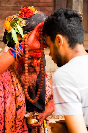 Pashupatinath, Nepal - July 17, 2018 : Holy Sadhu man with traditional painted face and colouful clothes is blessing people at Pashupatinath, a famous and sacred Hindu temple complex in Nepalのeditorial素材