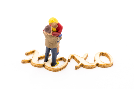 Miniature figures as in love hugging couple next to wooden sign with text XOXO, isolated on white backgroundの写真素材