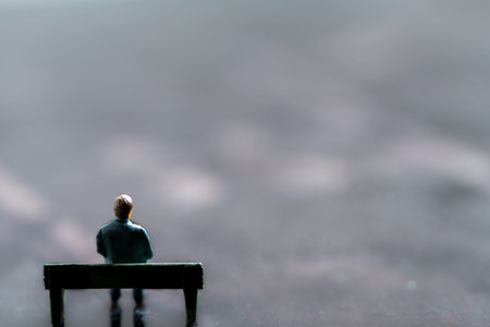 Miniature figurine posed as man sitting alone on a bench in surreal scenery, minimalist abstract...