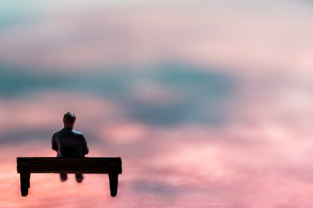 Miniature figurine posed as man sitting alone on a bench in surreal scenery, minimalist abstract concept imageの写真素材