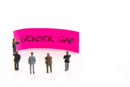 Meeting with miniature figurines posed as business people standing around sticky note with Gender Gap handwritten message in background, minimalist abstract concept with focus on textの写真素材