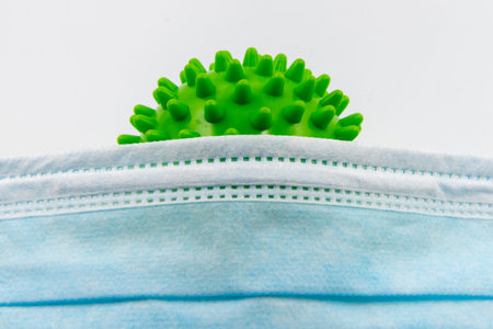 Closeup on single use medical face mask and spiky ball as coronavirus representation isolated over...