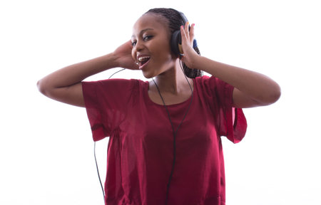 African woman with braids is happily listening to music through earphones on an isolated white...