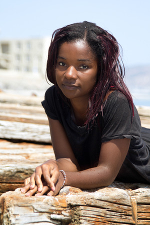 Close-up portrait of a beautiful ethnic woman with a shirt on lying on a strip of wood on the beachの写真素材