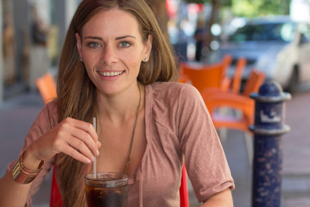 Caucasian female sitting outside a cafe enjoying a glass of soda