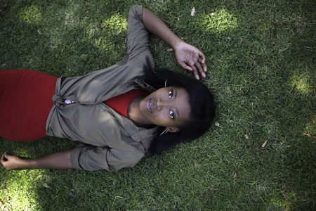 A young brunette African model poses while laying on a lawn whilst looking directly at the cameraの写真素材