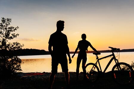 couple on a bicycle at sunset by the lakeの写真素材
