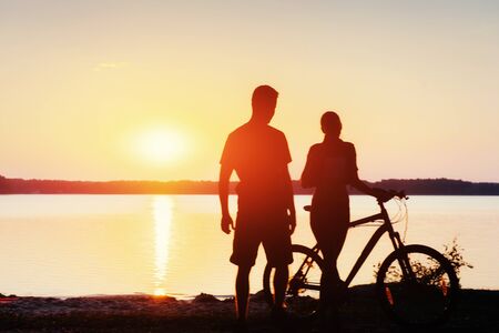 couple on a bicycle at sunset by the lakeの写真素材