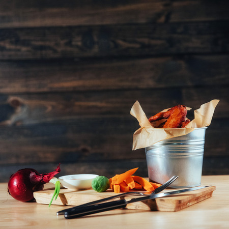 harnished chicken wings with sauce and vegetables on wooden tableの写真素材