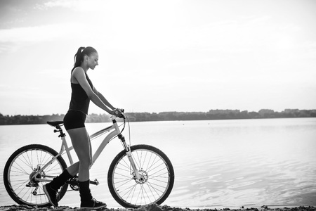 Charming girl in sportswear with a bicycle near the waterの写真素材