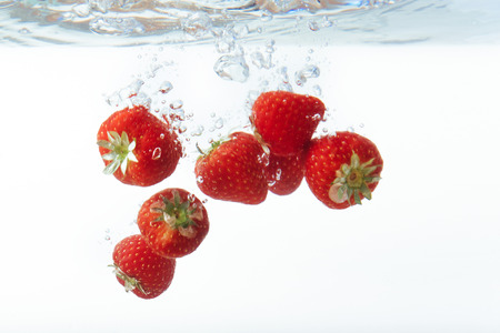 fresh strawberry dropped into water with splash on white backgroの写真素材