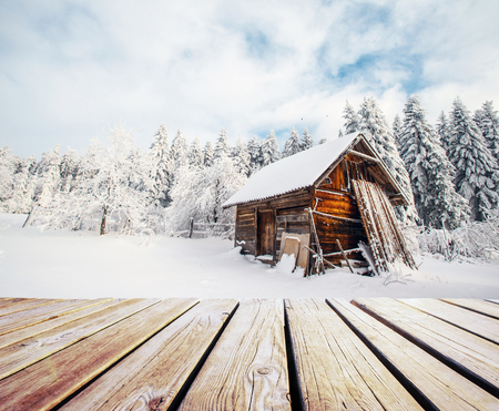winter mountains landscape with a snowy forest and a wooden hut and shabby table.の写真素材