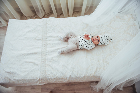 Newborn baby dressed in a white suit and black stars is a white soft bed in the studio.の写真素材
