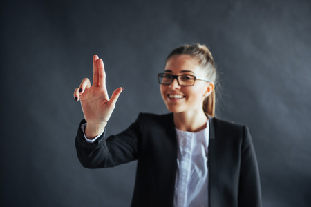 Happy business woman shows finger up, standing on a black background in the studio, friendly, smiling, focus on hand.の写真素材