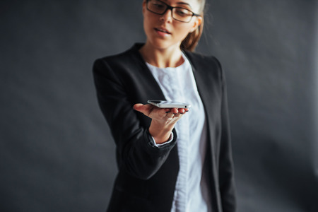 Portrait of cheerful woman showing a smartphone on a black background. Focus on a smartphone in hand.の写真素材