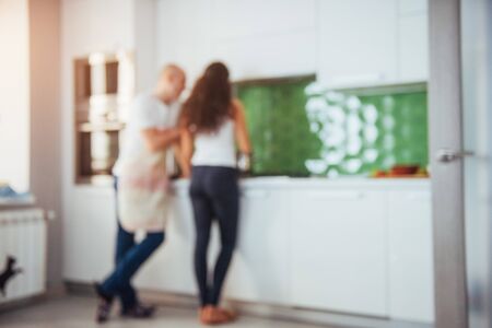 Beautiful young couple is talking, looking at camera and smiling while cooking in kitchen.の写真素材