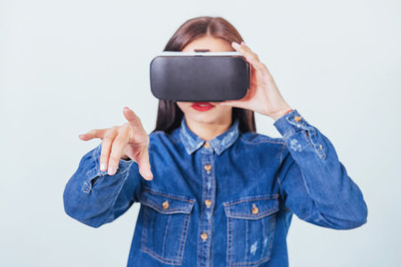 brunette beautiful woman posing in the studio, wearing jeans wear, using VR-glasses virtual reality...