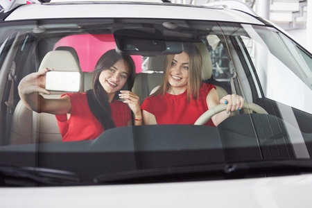 Enjoying travel. Beautiful young girl twins sitting on the front passenger seats and smiling while...
