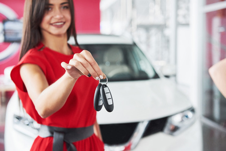 Smiling car salesman handing over your new car keys, dealership and sales concept. Happy girl the buyerの写真素材