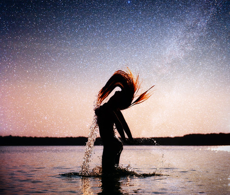 woman on water background at night sky. Fantastic starry sky and the milky wayの写真素材