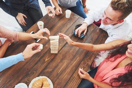 Top view creative photo of friends sitting at wooden table. Friends having fun while playing board...