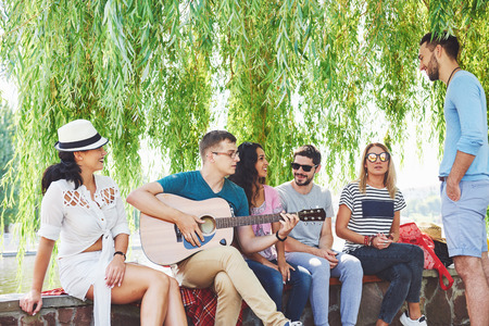 Group of happy friends with guitar. While one of them is playing guitar and others are giving him a round of applauseの写真素材
