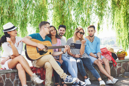 Group of happy friends with guitar. While one of them is playing guitar and others are giving him a...