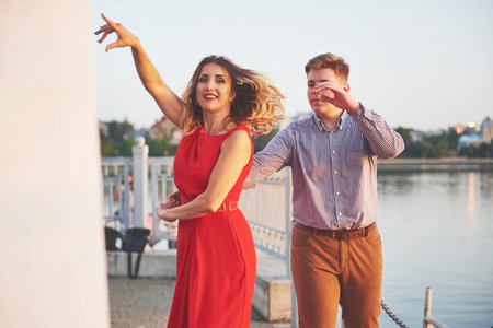 Happy beautiful woman in red dress and young man dance of on summer with lake in the background....