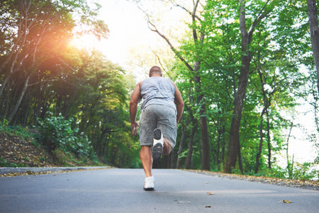 Outdoor cross-country running in concept for exercising, fitness and healthy lifestyle. Close up of feet of young runner man running along road in the park.の写真素材