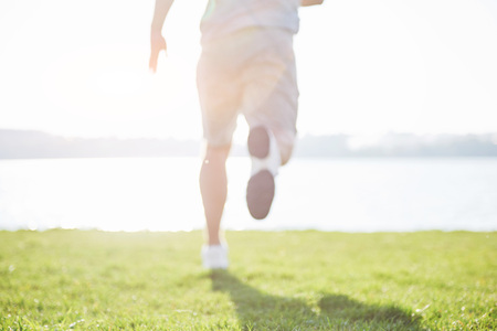 Outdoor cross-country running in summer sunshine concept for exercising, fitness and healthy lifestyle. Close up of feet of a man running in grass.の写真素材