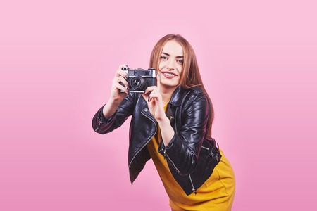 Fashion look, pretty cool young woman model with retro film camera wearing a black jacket, against pink background with copy space.の写真素材