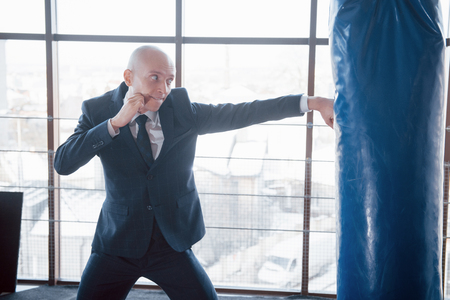 An angry bald businessman beats a boxing pear in the gym. concept of anger management.の写真素材