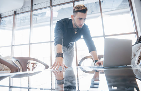 Conceived young man working on laptop while sitting at his working place in office.の写真素材