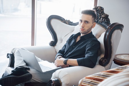 young businessman working on modern loft office. Man wearing white shirt and using contemporary laptop. Panoramic windows background.の写真素材