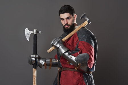 Medieval knight on grey background. Portrait of brutal dirty face warrior with chain mail armour red...