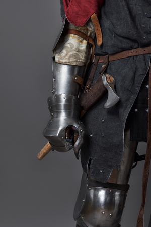 Medieval knight on grey background. Portrait of brutal dirty face warrior with chain mail armour red and black clothes and battle axe.の写真素材