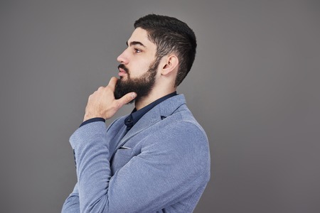 Portrait in profile of freelancer man with beard in jacket standing against gray backdrop.の写真素材