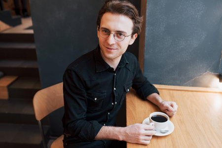 Handsome bearded man in checked shirt holding fork eating in cafe and smiling looking at camera.