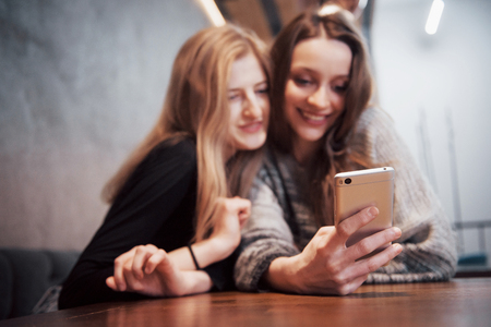 One-on-one meeting.Two young business women sitting at table in cafe.Girl shows her friend image on screen of smartphone. On table is closed notebook.Meeting friends.の写真素材