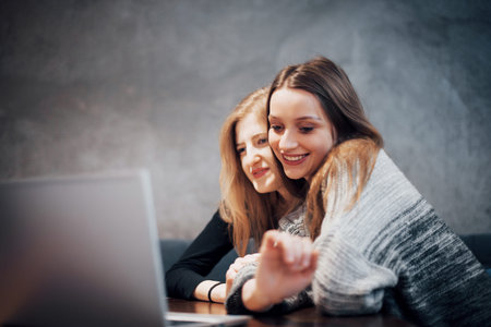 Two girls surfing the net, posting on social networks on a laptop computer and having fun.の写真素材