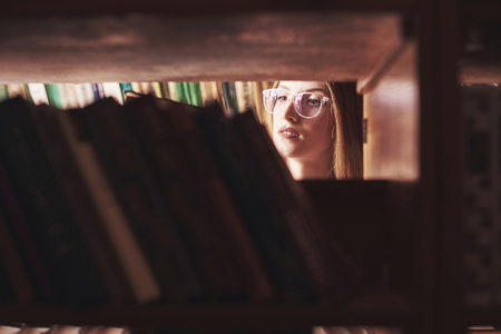 A young student girl is looking for the right book on the shelves of the old university library.の写真素材