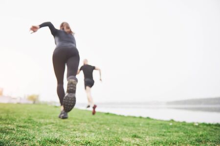 Couple jogging and running outdoors in park near the water. Young bearded man and woman exercising together in morning.の写真素材