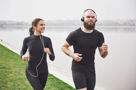 Profile view image of an athletic couple wearing arm bands with smart phones and headphones. Young...
