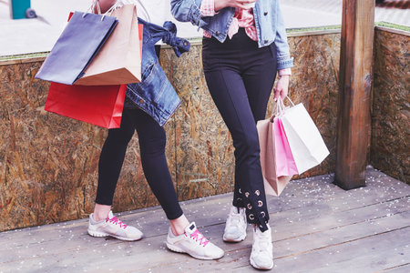 Two young woman carrying shopping bags while walking in the street after visiting the stores.